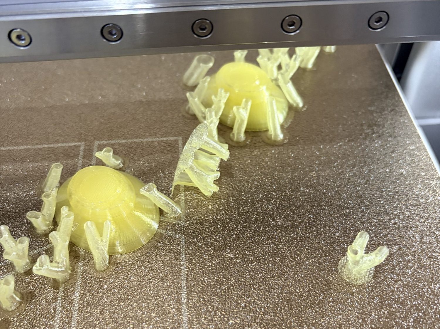 Inside the printer, looking down at the bed: two round yellow feet with thin branching supports around them, several supports knocked over and lying loose