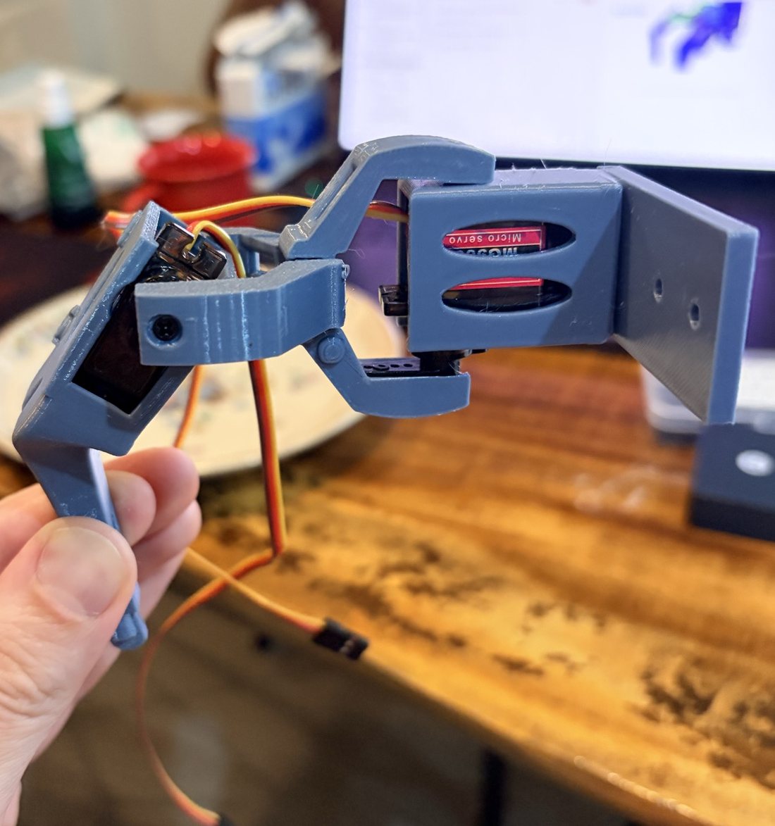 The whole printed leg hanging from its blue hip block, with the hip and knee servos and their orange cables