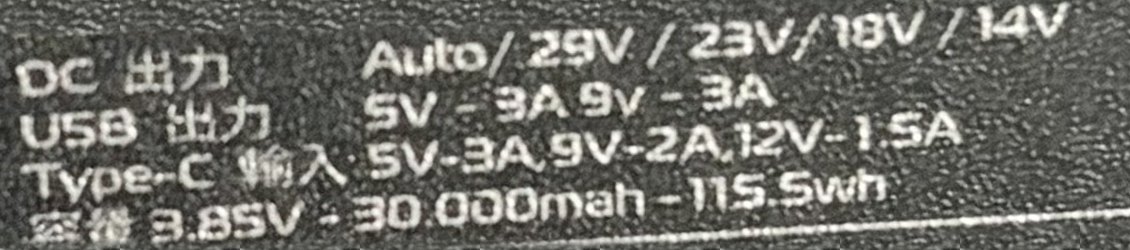 Close-up of the white print on a black power bank label. The USB output row reads 5V-3A 9V-3A; the Type-C input row reads 5V-3A, 9V-2A, 12V-1.5A; the capacity row reads 3.85V, 30,000 mAh, 115.5 Wh