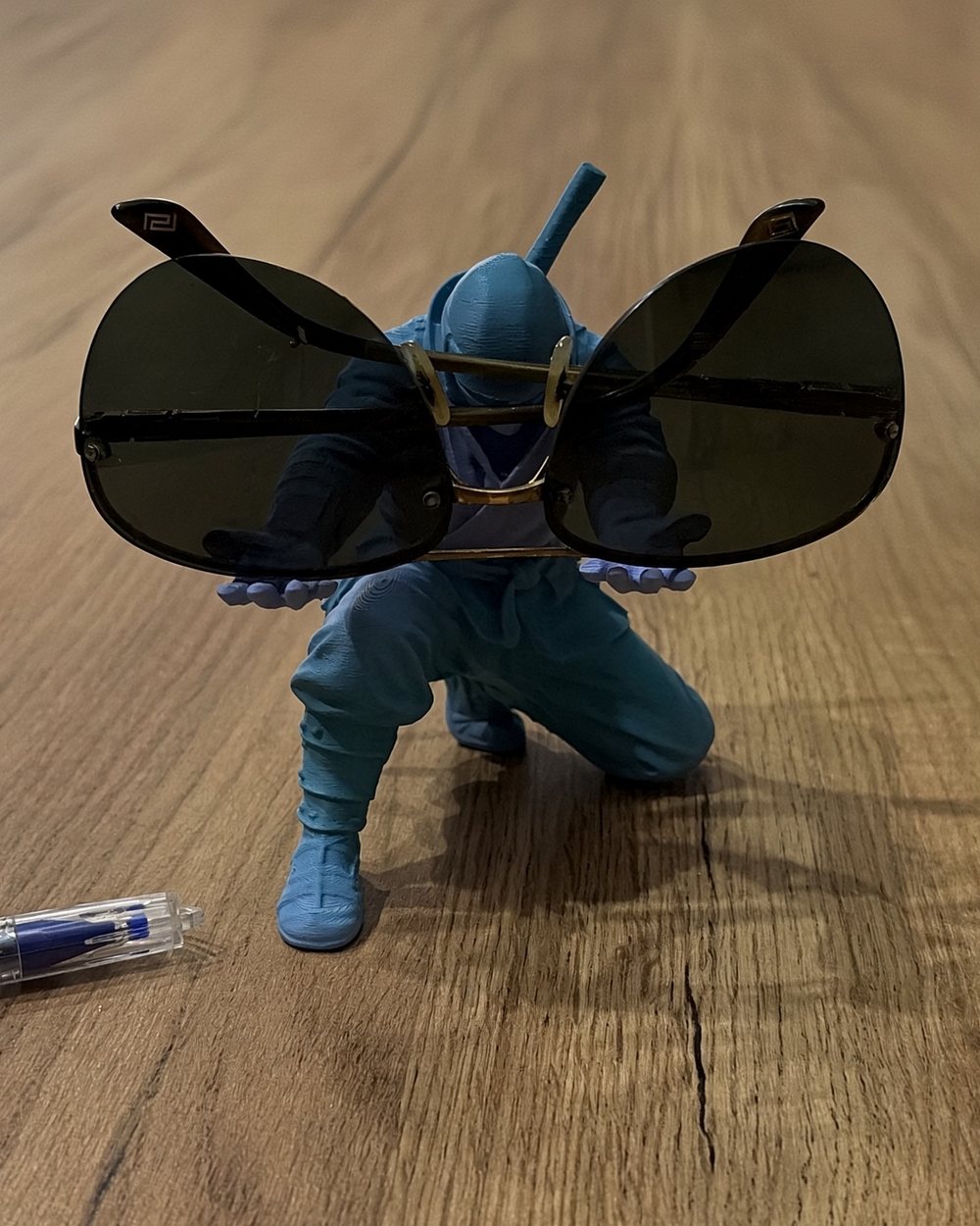 Ninja xanh ngồi trên bàn gỗ, hai tay giơ cặp kính râm